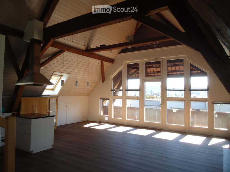 Bright, open attic space with wooden beams, large windows, skylight, and modern kitchen island.