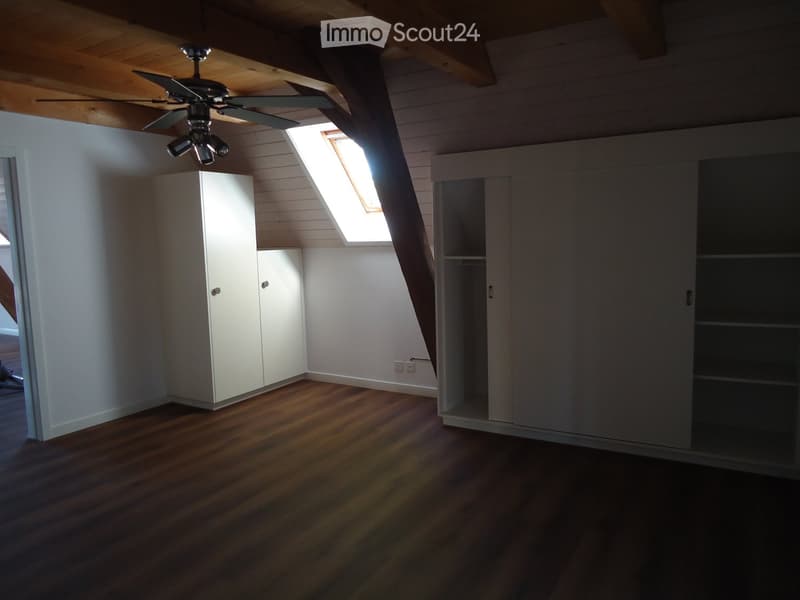 Empty attic room with wooden floors, white walls, built-in cabinets, and a skylight window.