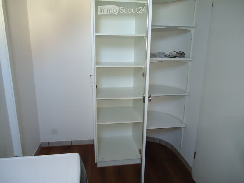 Empty room with white built-in shelving unit, wooden floor, and white walls.