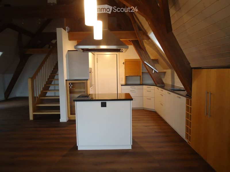 Modern kitchen with white cabinets, a central island, and wooden flooring. Features a range hood, stove, and wine rack.