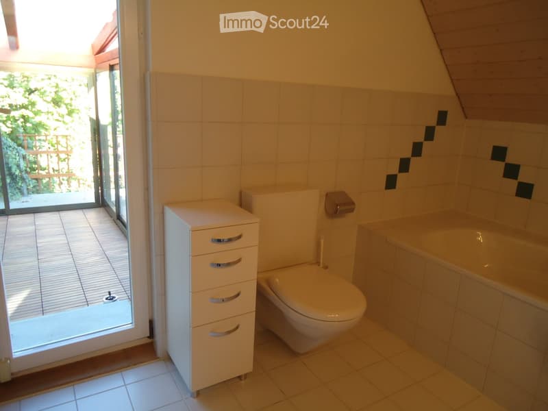 Bathroom with a toilet, bathtub, and a white storage cabinet. The room has tiled walls and a large window opening to a balcony.