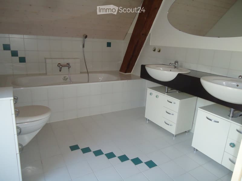 Modern bathroom with white tiles, a bathtub, toilet, double sink, and white cabinets.