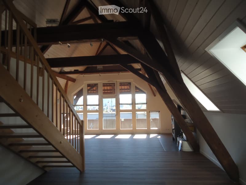Open, airy attic space with wooden beams, wooden staircase, large windows, and wooden flooring.