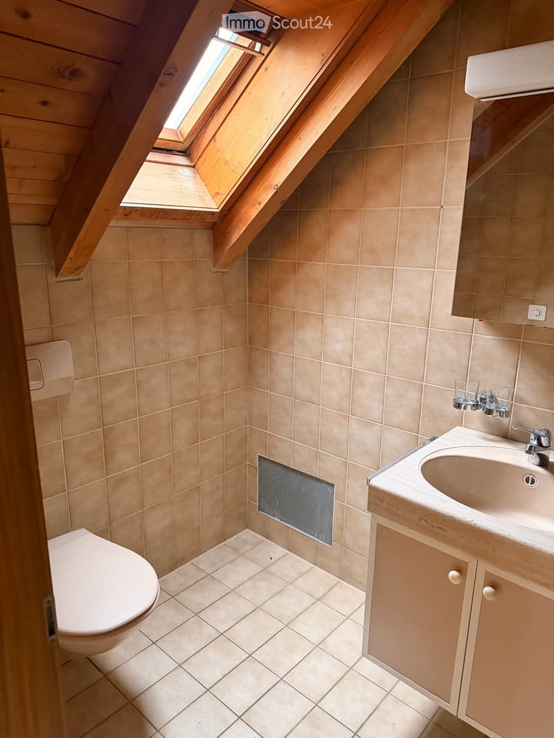 Small bathroom with beige tiles, a toilet, a sink with a mirror, and a window letting in natural light.