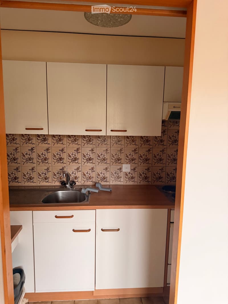 A small kitchen with white cabinets, a stainless steel sink, and floral-patterned tiles on the backsplash.