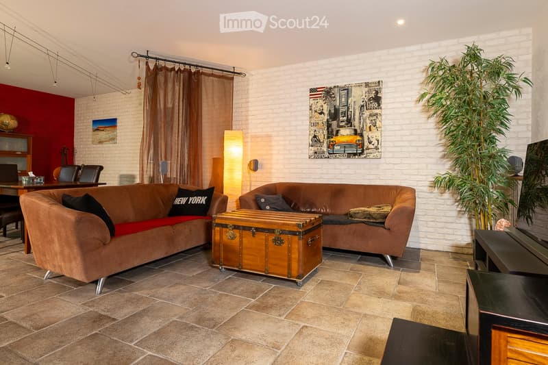 Living room with a brown leather sofa, coffee table, chairs, a large plant, and artwork on the walls.