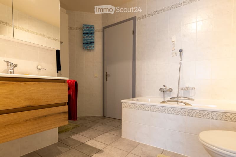 Modern bathroom with a bathtub, sink, and toilet. Features tiled walls, a wooden vanity, and a decorative border along the bathtub.
