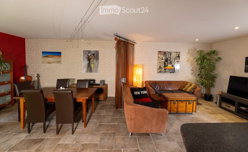 A well-furnished room with a mix of seating and dining areas. Features include a brown leather sofa, wooden dining table with chairs, a guitar, a floor lamp, a television, and decorative plants.