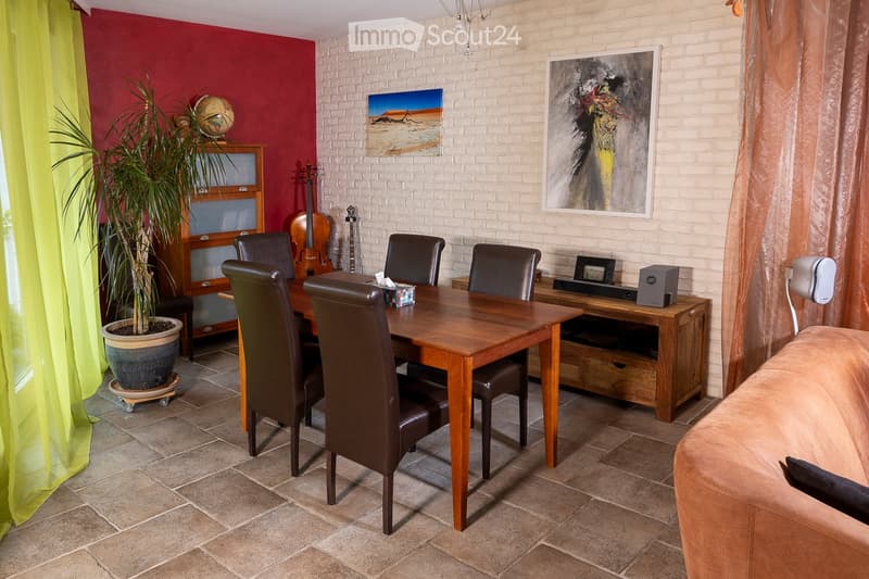 A well-furnished room with a dining table and chairs, a sofa, a guitar, a potted plant, and a speaker system. The room features a mix of modern and rustic decor, including a brick wall, wooden furniture, and colorful artwork.