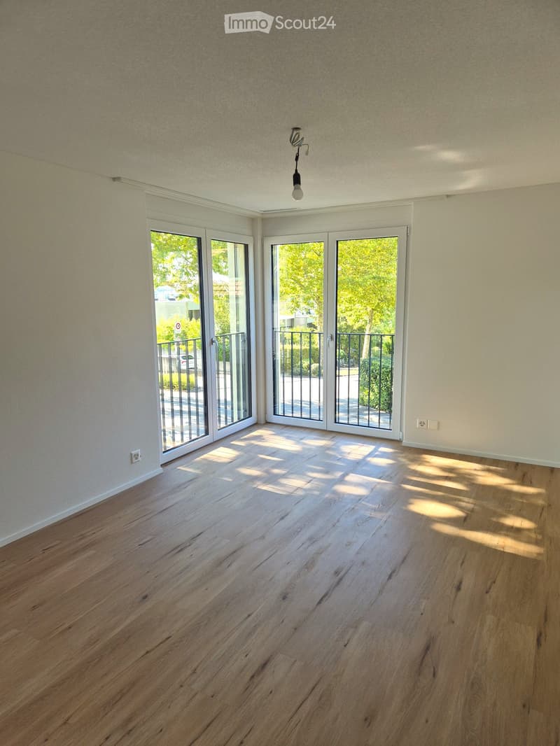 Empty room with wooden flooring, large glass doors leading to a balcony, and natural light streaming in.