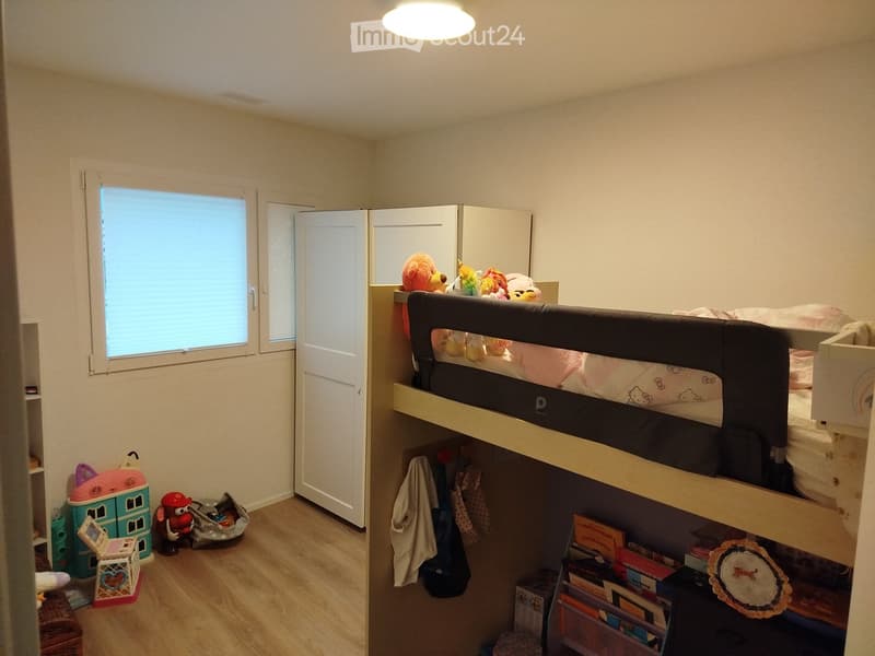 Cozy children's bedroom with a bunk bed, wardrobe, bookshelf, and various toys and storage boxes.