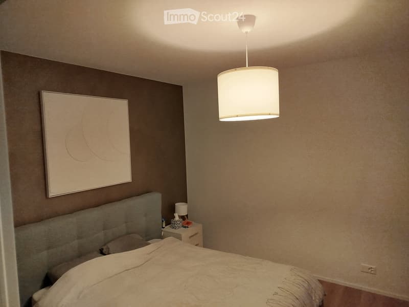 Modern bedroom with a large bed, nightstand, lamp, and a decorative picture frame on the wall.