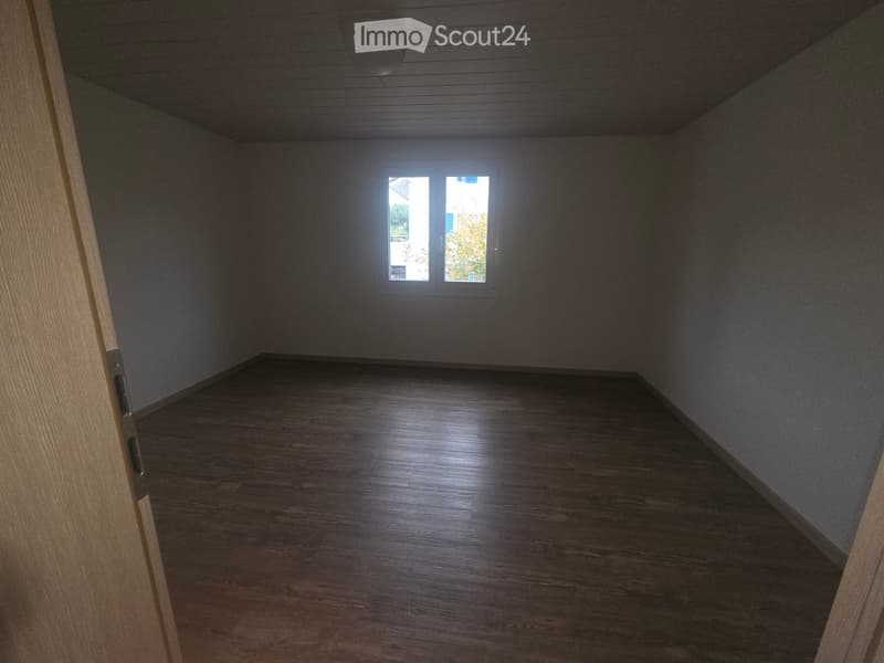 Empty room with wooden flooring, grey walls, and a window letting in natural light.