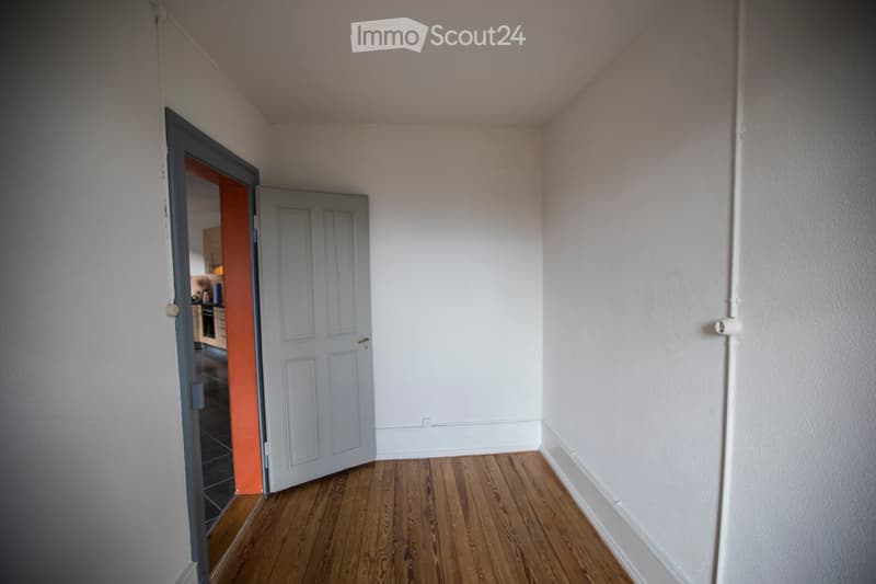 Empty room with wooden flooring, white walls, and a partially open door leading to another room.