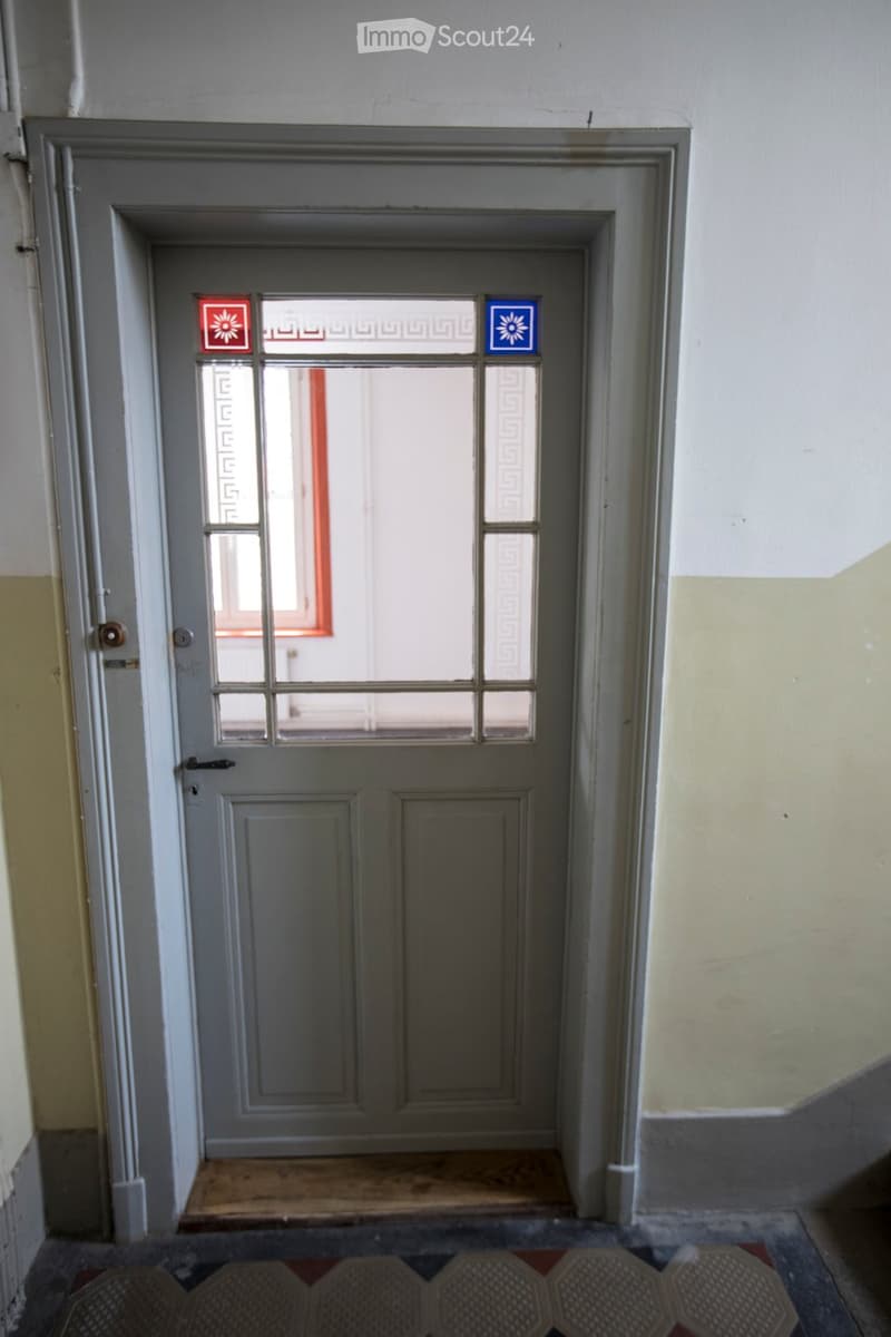 Grey door with glass panels and decorative designs, set in a simple frame with a small step leading up to it.