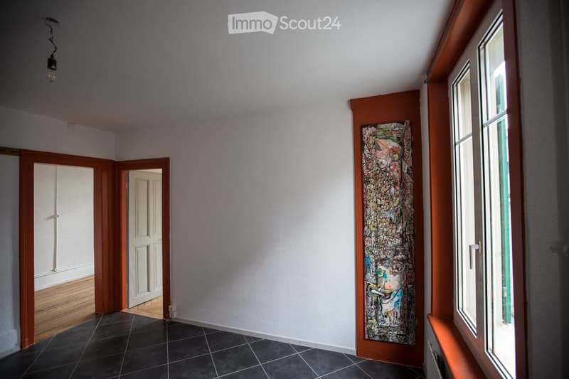 Empty hallway with white walls, dark tiled floor, wooden doors, and a colorful abstract painting on one wall.