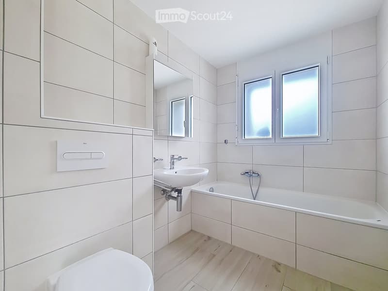 Modern bathroom with white tiles, a toilet, a sink, a bathtub, a mirror, and a cabinet.