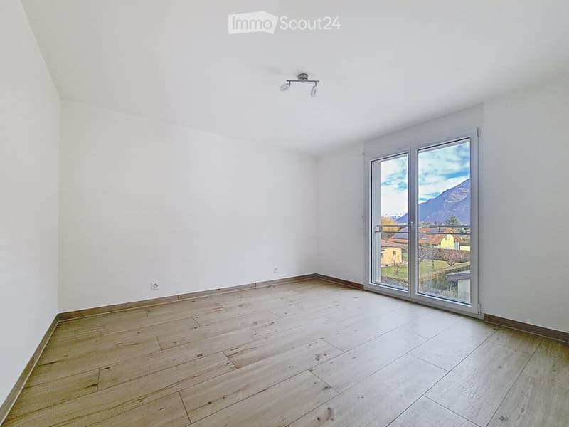 Empty room with light-colored wooden flooring and white walls, featuring a large sliding glass door leading to a balcony with a scenic mountain view.