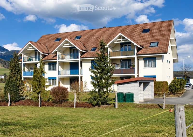 A two-story house with a red-tiled roof, white walls, multiple balconies, and surrounding greenery.