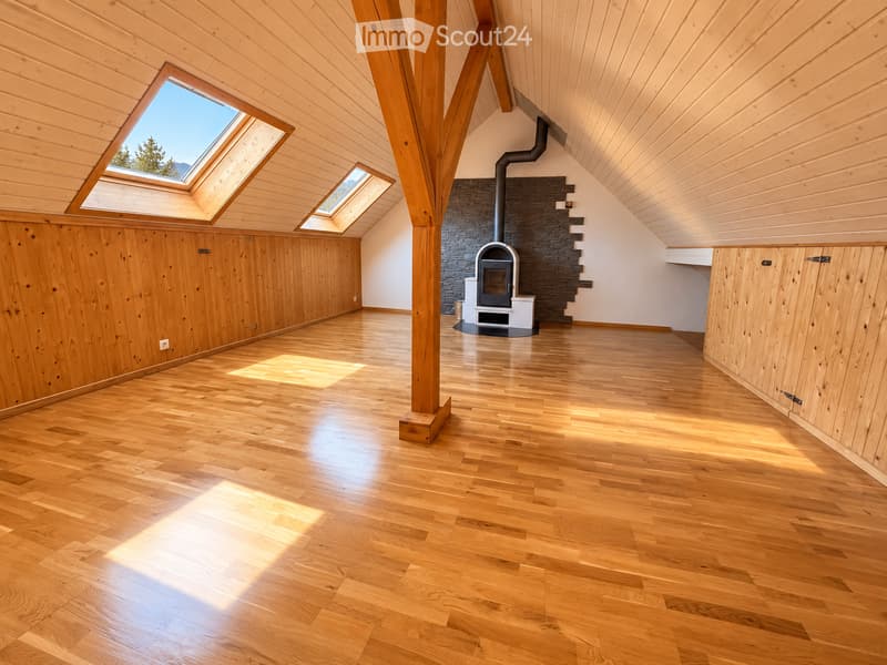 Bright, empty attic space with wooden floors, exposed wooden beams, skylights, and a modern fireplace.