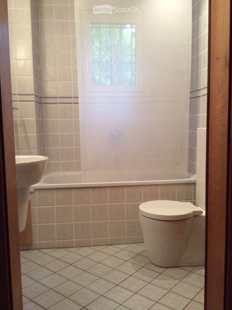 Bathroom with beige tiled walls and floor, featuring a toilet, bathtub, and sink.