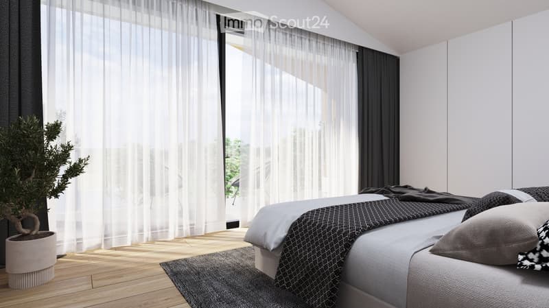 Modern bedroom with a grey bed, patterned blanket, pillows, a grey rug, and a potted plant near the window with sheer curtains.