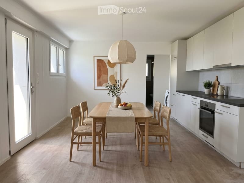 Bright, modern dining area with a wooden dining table, six chairs, pendant light, and a small kitchen area with white cabinets, an oven, and a washing machine.