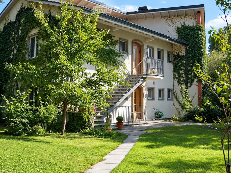Two-story house with white exterior, covered balcony, ivy-covered walls, and a well-maintained garden with a pathway leading to the entrance.