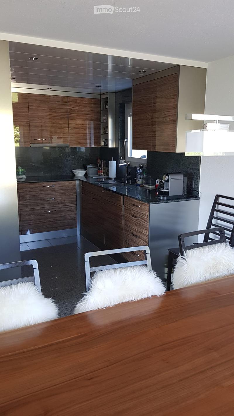Modern kitchen with wooden cabinets, black countertops, stainless steel appliances, and a dining area with a wooden table and chairs.