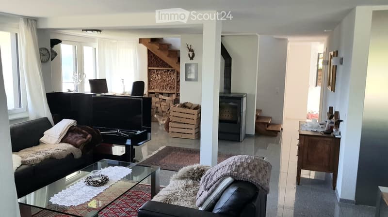 Modern living room with a black leather sofa, glass coffee table, fireplace, and a staircase leading to the upper level.