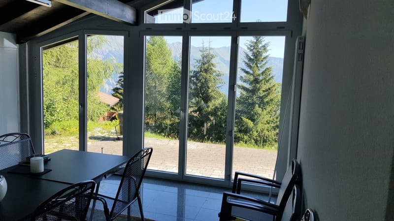 Bright room with large windows offering a scenic mountain view, featuring a table and chairs.