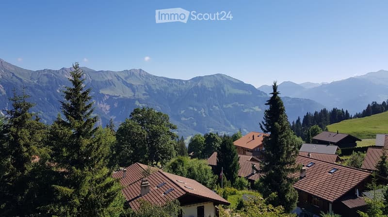 A picturesque village nestled in a lush green valley with traditional houses and red-tiled roofs, surrounded by towering mountains under a clear blue sky.