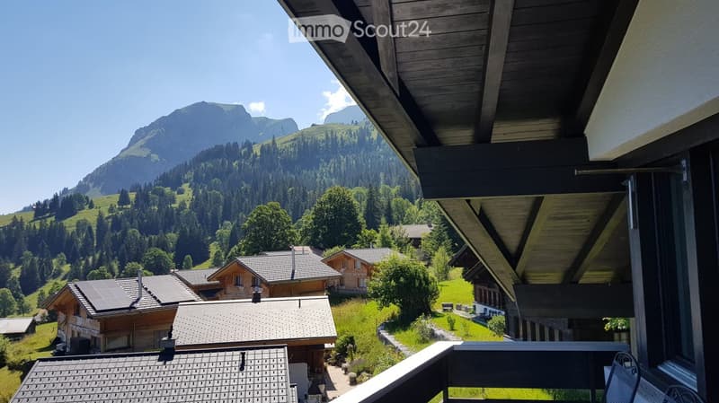 Balcony overlooking a scenic mountain valley with traditional wooden houses and lush greenery.