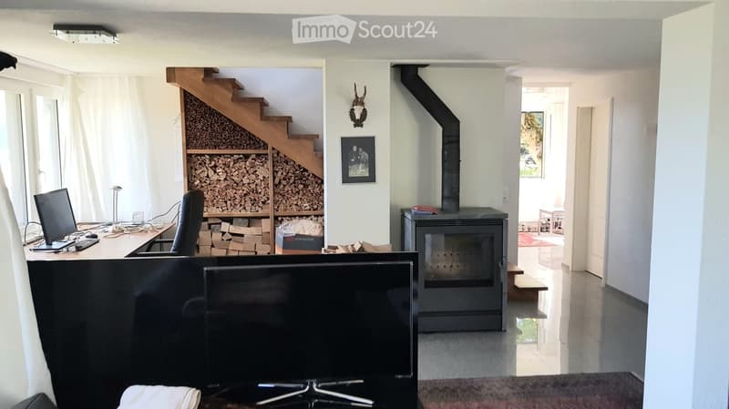 Spacious room with a fireplace, a desk with a computer, a large screen, and a staircase leading to a wood storage area.