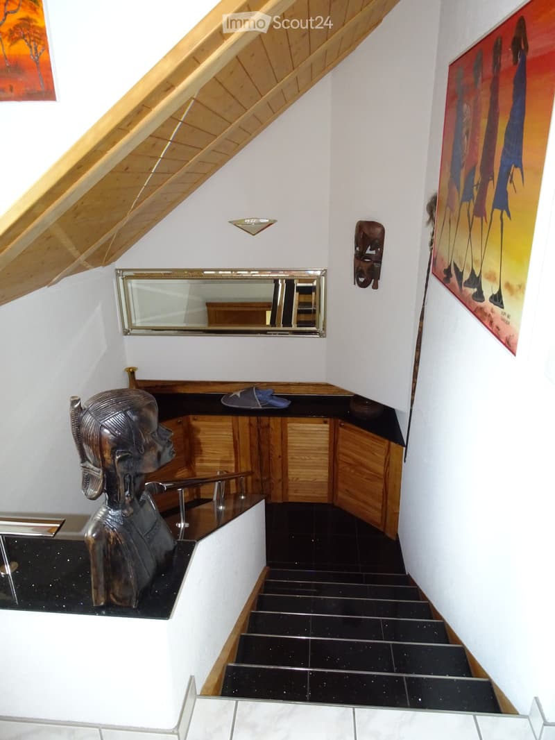 Staircase with black tiled steps, wooden handrail, and black countertop with a small cabinet, featuring decorative items like sculptures and artwork on the walls.