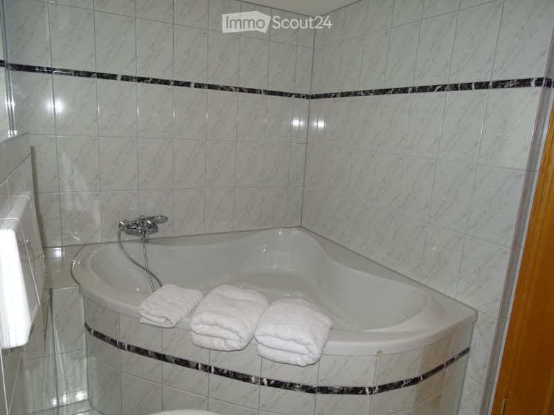 Bathroom with a white bathtub, marble tiles, and three folded white towels placed on the edge of the tub.
