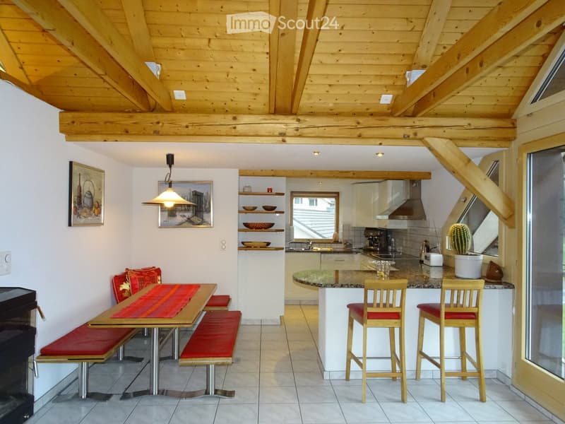 Open-plan living and dining area with a wooden table, red bench seating, bar stools, kitchen island, and modern appliances.