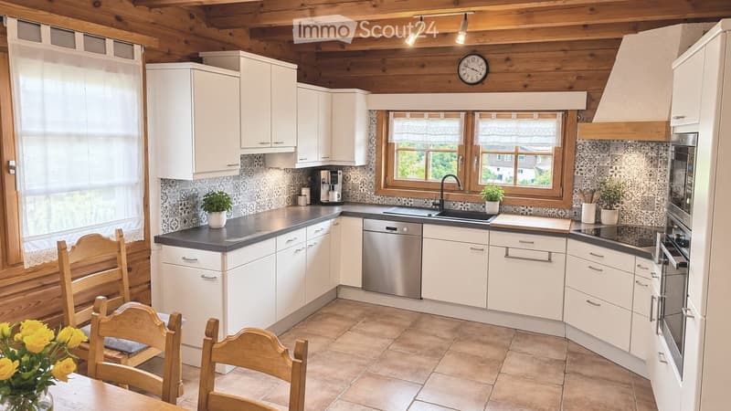 Bright kitchen with white cabinets, dark countertops, and wooden accents. Features include a sink, dishwasher, oven, refrigerator, and a small dining area with chairs and a table.