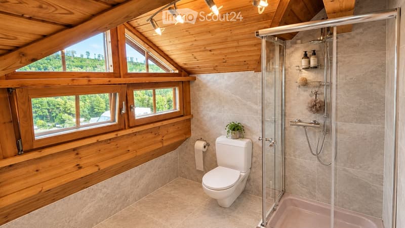 Bathroom with wooden ceiling, large windows, toilet, glass-enclosed shower, and decorative plant on the toilet tank.