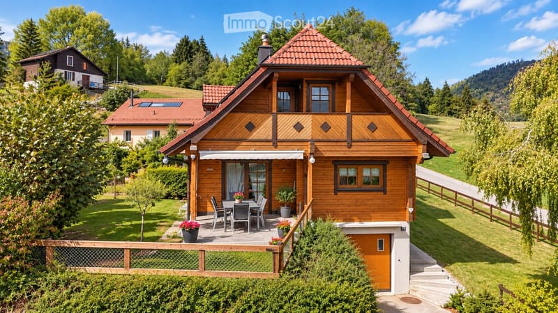 Two-story wooden house with red-tiled roof, balcony, and outdoor seating area with a table and chairs.