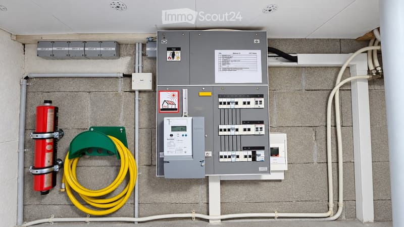 Electrical panel with multiple circuit breakers, a fire extinguisher, and a coiled yellow cable mounted on a wall.