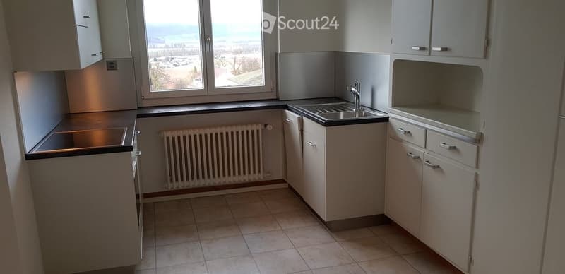 Modern kitchen with white cabinets, tiled floor, sink, faucet, and radiator under large windows offering a scenic view.