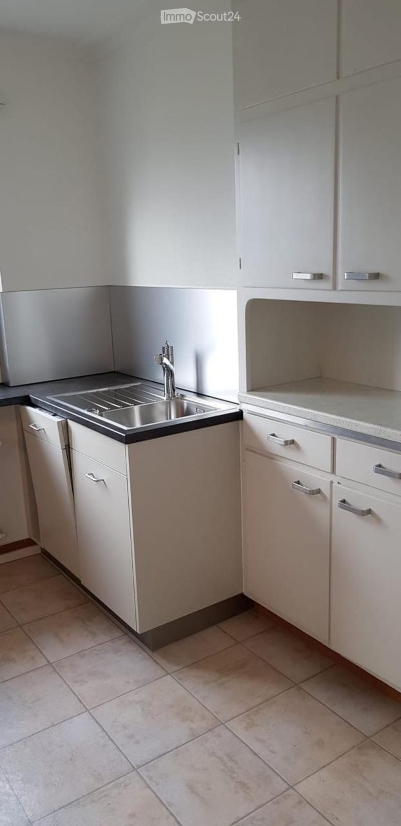 Modern kitchen with white cabinets, stainless steel sink, and beige tiled floor.