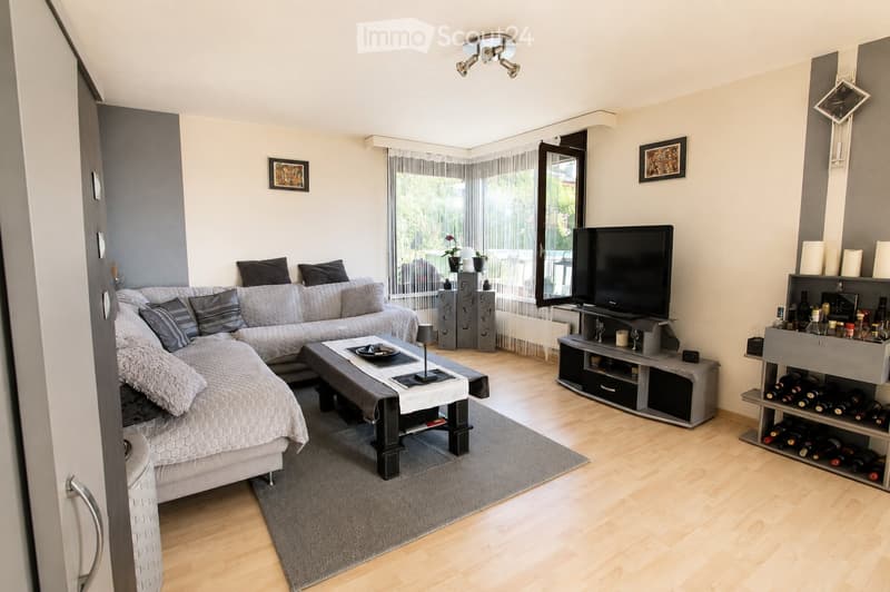 Modern living room with a grey sectional sofa, coffee table, flat-screen TV, wine rack, and decorative items.