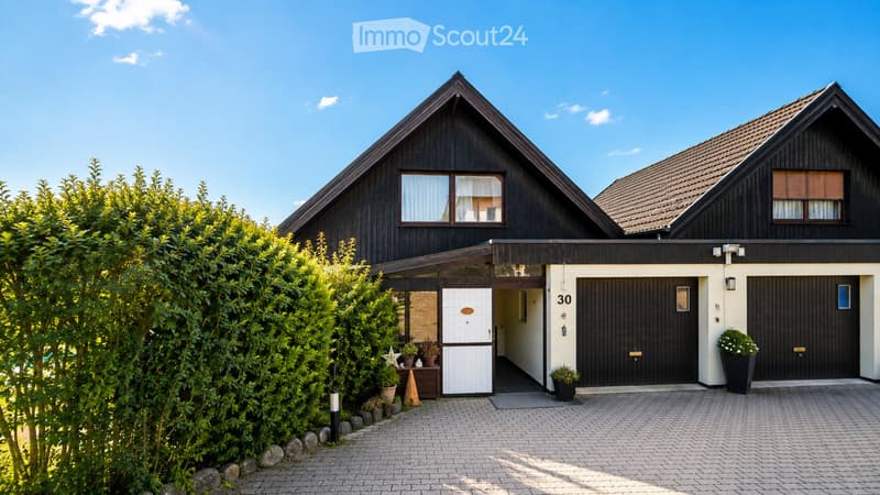 Two-story house with dark wooden exterior, white garage door, and small porch area with potted plants.
