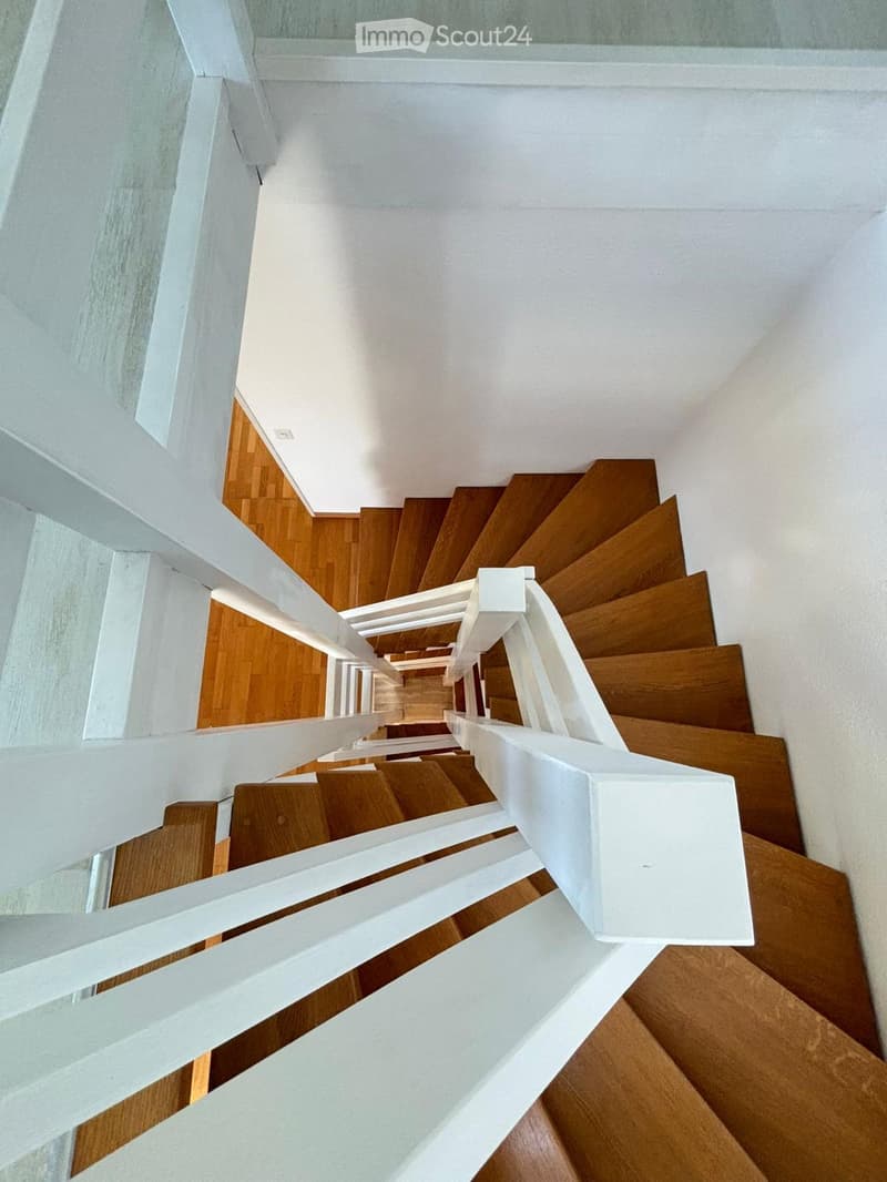 Spiral staircase with wooden steps and white railings, leading upwards in a modern interior.