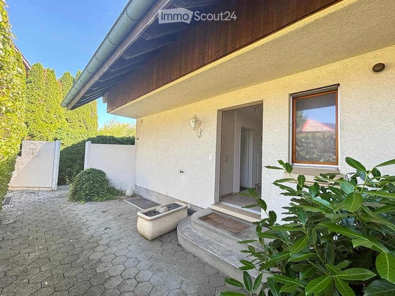 Garden area with a paved walkway, steps leading to a house entrance, potted plants, and surrounding greenery.