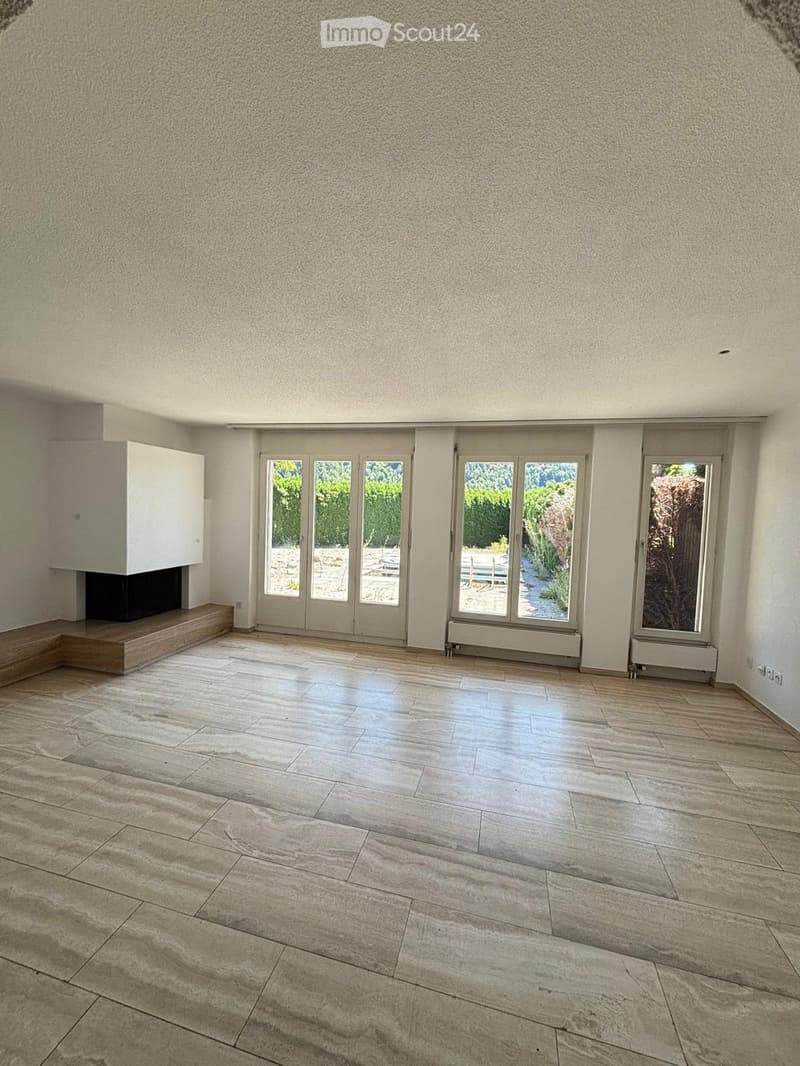 Empty room with light-colored tiled flooring, large glass doors leading to an outdoor area, and a built-in fireplace on the left side.