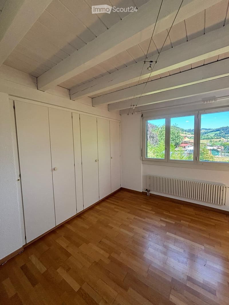 Empty room with wooden flooring, white walls, large windows offering a scenic view, and a radiator below the windows.