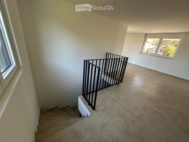 Empty hallway with tiled floor, white walls, and a staircase leading upwards with a black metal railing. Two windows provide natural light.